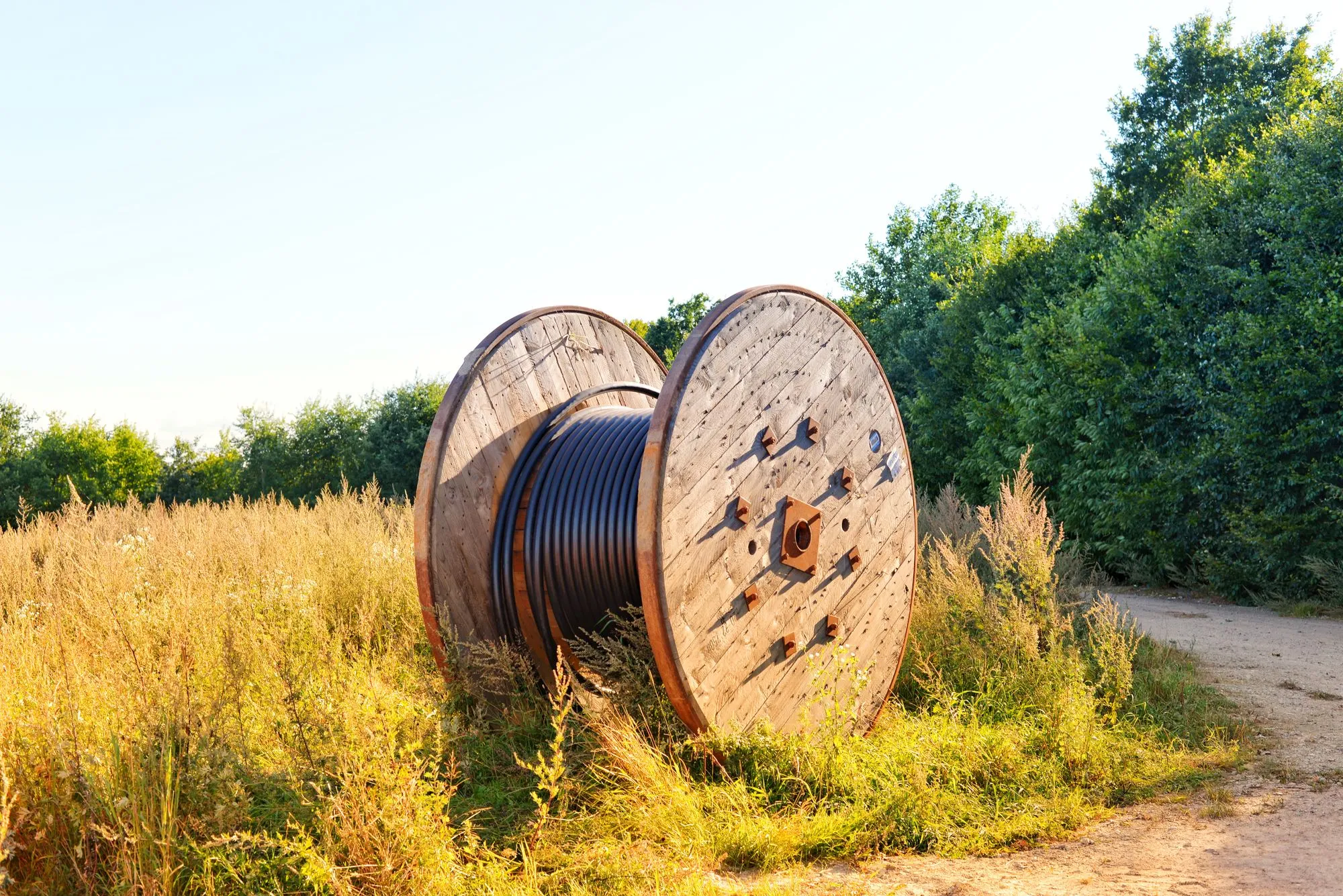 Wooden cable reel wound with black cable, standing in a field