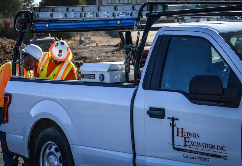 Hudson Excavation crew members in hard hats and safety vests working beside a company pickup truck