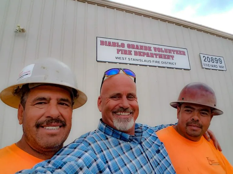 Three Hudson Excavation team members smiling together outside a job site building